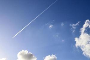 Aircraft condensation contrails in the blue sky inbetween some clouds photo