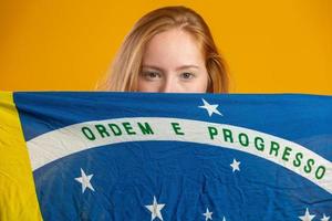 Mysterious redhead woman fan holding a Brazilian flag in your face. Brazil colors in background, green, blue and yellow. Elections, soccer or politics. photo