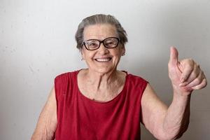 Beautiful old woman with two tumbs up. Cheerful caucasian senior showing two thumbs up on white background. photo