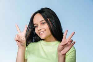 Portrait of a smiling happy woman showing victory sign and looking at camera on the blue background. photo