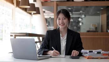 Beautiful smiling Asian woman working at the office, looking at the camera. photo