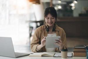 Asian woman wearing headphones around her neck using laptop and recording homework from teacher photo