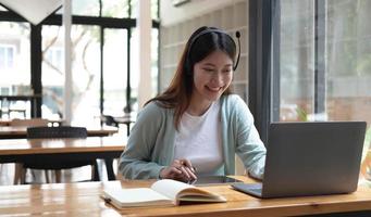 mujer joven feliz con auriculares hablando mirando la computadora portátil tomando notas, estudiante hablando por videoconferencia, profesora tutora por cámara web, capacitación en línea, concepto de entrenamiento electrónico foto