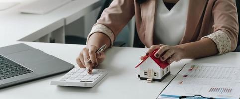 businesswoman with house model doing finances and calculate about cost to real estate investment and in other, tax system. Business Financing Accounting Banking Concept photo