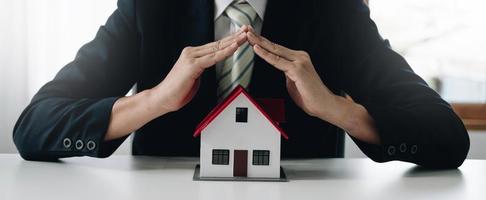 una pequeña casa modelo gris es un ejemplo de una casa en un proyecto de vivienda, un vendedor de seguros está haciendo un acto simbólico de protección del hogar en el seguro del hogar. concepto de arrendamiento de bienes raíces. foto