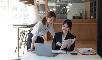 Two young asian women colleagues in smart casual wear planning business strategy together at the modern coworking space.
