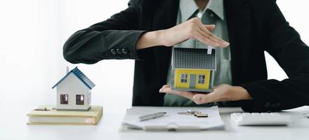 casa en miniatura en manos de una mujer asiática agente de bienes raíces préstamo hipotecario que trabaja en la oficina. foto