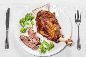 Top view lamb meat baked on a bone on a white plate with broccoli