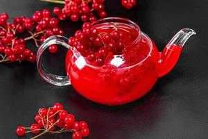 Drink in a glass teapot with fresh viburnum berries on a black background photo