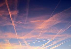 Aircraft condensation contrails in the blue sky inbetween some clouds photo