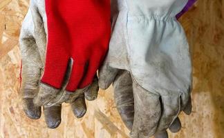 Two pairs of old leather work gloves hang in front of wooden background. photo