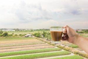 la mano de un hombre blanco sosteniendo una taza de café caliente en el fondo de la naturaleza del campo del paisaje. foto