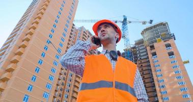 retrato de un especialista en construcción con casco naranja y chaleco de seguridad contra un gran edificio