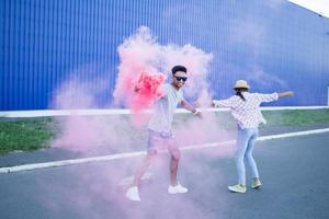 Young couple riding on skateboards with color smoke bomb, boy and girl in casual clothes having good time, pink and blue colors photo