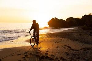silueta de un joven ciclista con casco en la playa durante la hermosa puesta de sol foto