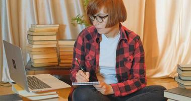 Young woman student studying at home with many books and laptop photo