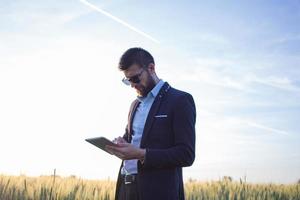 hombre de negocios en campos de trigo de verano usando tableta durante la puesta de sol, hombre de traje con computadora compacta foto