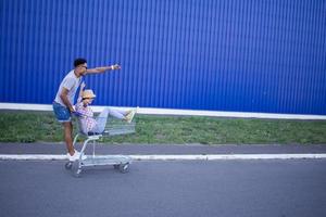 Happy young couple riding on trolley on empty mall parking , hipster friend have good time during shopping, couple in love riding on shopping cart photo