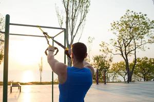 entrenamiento con correas de suspensión en el gimnasio al aire libre, entrenamiento de hombres fuertes temprano en la mañana en el parque, amanecer o atardecer en el fondo del mar