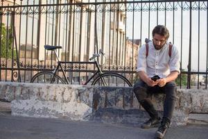 joven barbudo con mochila de cuero caminando con bicicleta negra foto