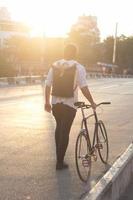 Young bearded man with leather backpack walking with black bicycle photo