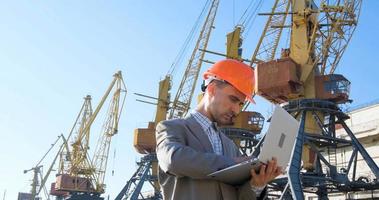 Young male worker of sea harbor in helmet, cargo manager in suit and halmet works outdoor , cranes and sea background photo