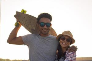 feliz pareja joven montando monopatín durante el amanecer foto