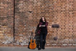 Young male with long hair and tattoo play on acoustic guitar outdoors on the street photo