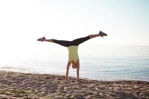 joven gimnasta profesional baila en la playa, entrena ejercicios con juncos frescos, amanecer en el fondo del mar o del océano foto