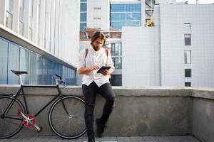 Young bearded man with leather backpack walking with black bicycle photo