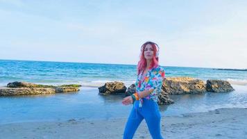 mujer joven con cabello colorido camina en la playa de verano y escucha música con auriculares