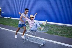 Happy young couple riding on trolley on empty mall parking , hipster friend have good time during shopping, couple in love riding on shopping cart photo