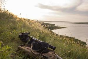 Photo camera on the baclpack and tripod in the mountainst against sunset and river