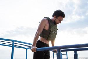 Young bearded athlete training outdoor with weighted vest, exercise with military plate carrier photo