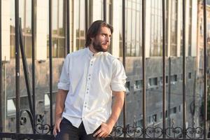 retrato de hombre barbudo con camisa blanca, fondo urbano, hipster posando en el puente foto