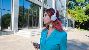 mujer joven con traje colorido y cabello rosado bebe café y escucha música en el parque foto