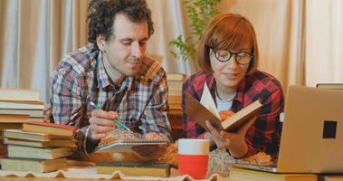 pareja joven estudia en casa con muchos libros y computadoras foto