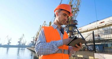 male worker of sea harbor in orange helmet and safety west, cranes and sea background photo