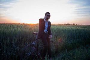 A caucasian businessman riding a bicycle in summer fields, Male in business suit ride on fixie bike. photo