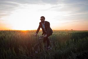 un hombre de negocios caucásico montando una bicicleta en los campos de verano, un hombre con traje de negocios montando en bicicleta fixie. foto