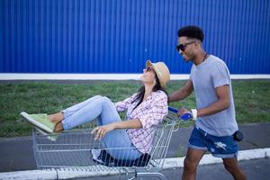 Happy young couple riding on trolley on empty mall parking , hipster friend have good time during shopping, couple in love riding on shopping cart photo