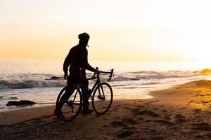silueta de un joven ciclista con casco en la playa durante la hermosa puesta de sol foto