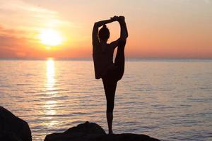 fitness mixed race asian woman in yoga pose on the morning beach, beautiful fit woman practice fitness exrxise stones, morning sea or ocean background photo