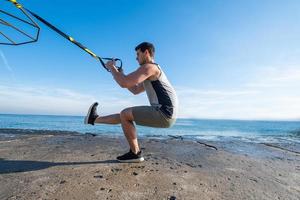 Fit male training on the summer, exercises with suspension straps outdoors photo