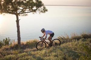 Bicycle rider on professional cyclocross bike ride downhill, pine and lake background photo