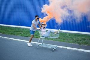 Happy young couple riding on trolley on empty mall parking , hipster friend have good time during shopping, couple in love riding on shopping cart photo