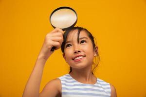 Portrait of happy little Asian child with magnifying glass. photo