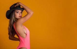 Attractive girl in a pink bikini, hat, emotionally opened mouth on a bright yellow background with a perfect body. Isolated. Studio shot.