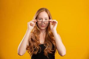 Beautiful young redhead woman with curly hair happy with her glasses. Eye care concept. On yellow background. photo