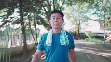 Asian mature man walking inside public park on sunny day, senior elderly Retirement life outdoor activity. Health care motivation, cool down exercise,  relaxing after work out, disease prevention video